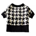 Black and white houndstooth knit dog sweater with ribbed collar and cuffs on wooden chair