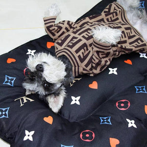 Small white dog lying on quilted designer dog bed with V monogram pattern and colorful accents