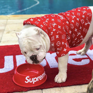 Bulldog eating from red Pupreme dog bowl with white logo on poolside mat